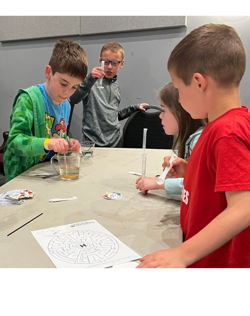 Kids gathered around a table running a hands-on science experiment with beakers and syringes.